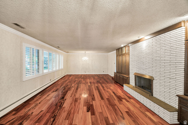 1365 Sumac Drive Logan, UT 84321 - Photo 11 of 66 Spacious living area featuring polished wood-finish flooring, an extensive white brick fireplace with a brass-toned insert, built-in wood cabinetry, a row of windows with plantation shutters, and crown molding