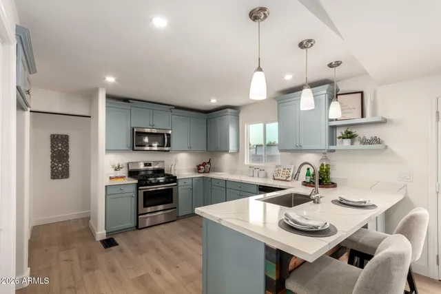 a kitchen with stainless steel appliances granite countertop a stove top oven a sink a refrigerator a center island and chairs