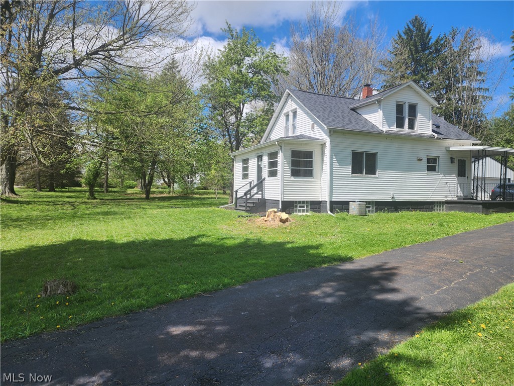 3187 Grenfall Road Barberton, OH 44203 - Photo 3 of 17 White siding exterior featuring a dark asphalt shingle roof, covered porch entrance, asphalt driveway, and expansive lawn with mature trees