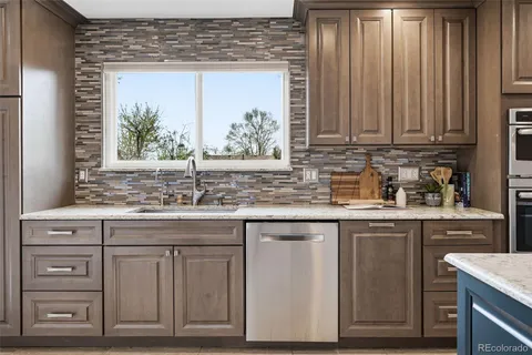 a kitchen with granite countertop wooden cabinets a sink and dishwasher next to a window