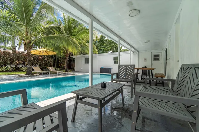 a view of a patio with couches table and chairs under an umbrella with large trees