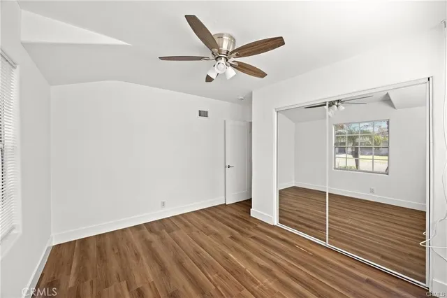 a view of an empty room with wooden floor and a ceiling fan