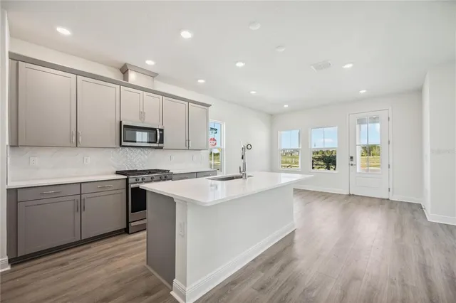 a kitchen with stainless steel appliances a sink dishwasher a stove and white cabinets with wooden floor