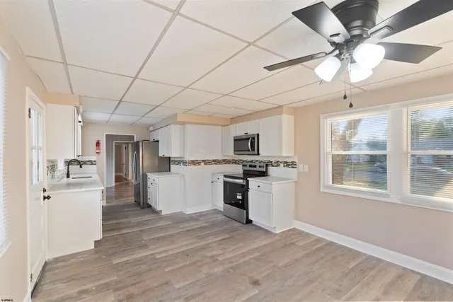 a kitchen with stainless steel appliances a stove top oven a sink a refrigerator white cabinets and wooden floor