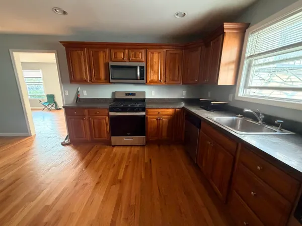a kitchen with wooden floors wooden cabinets stainless steel appliances a window and a sink