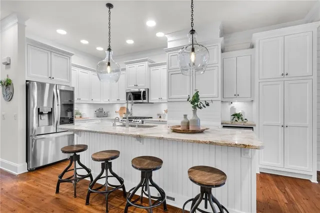 a kitchen with stainless steel appliances granite countertop a sink a stove a refrigerator and chairs