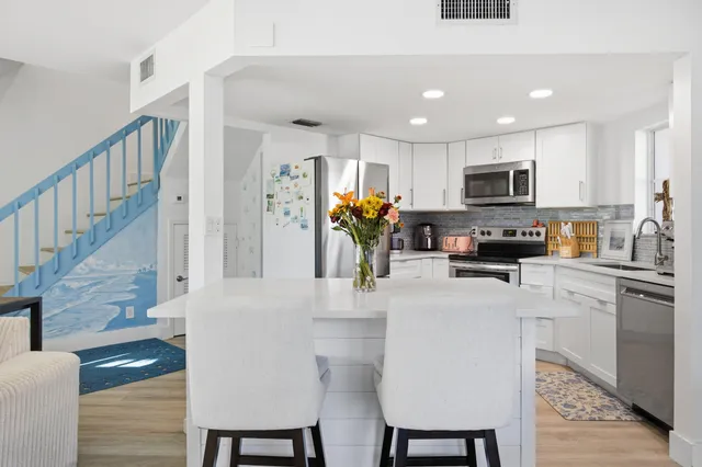 a kitchen with stainless steel appliances granite countertop a refrigerator a stove top oven a sink dishwasher and white cabinets with wooden floor