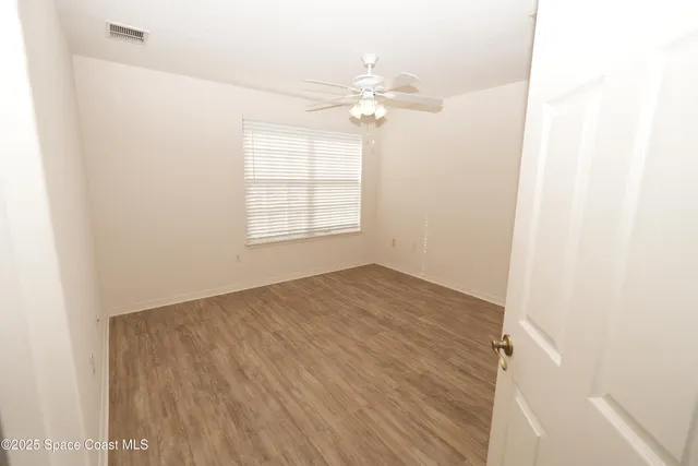 an empty room with wooden floor fan and windows