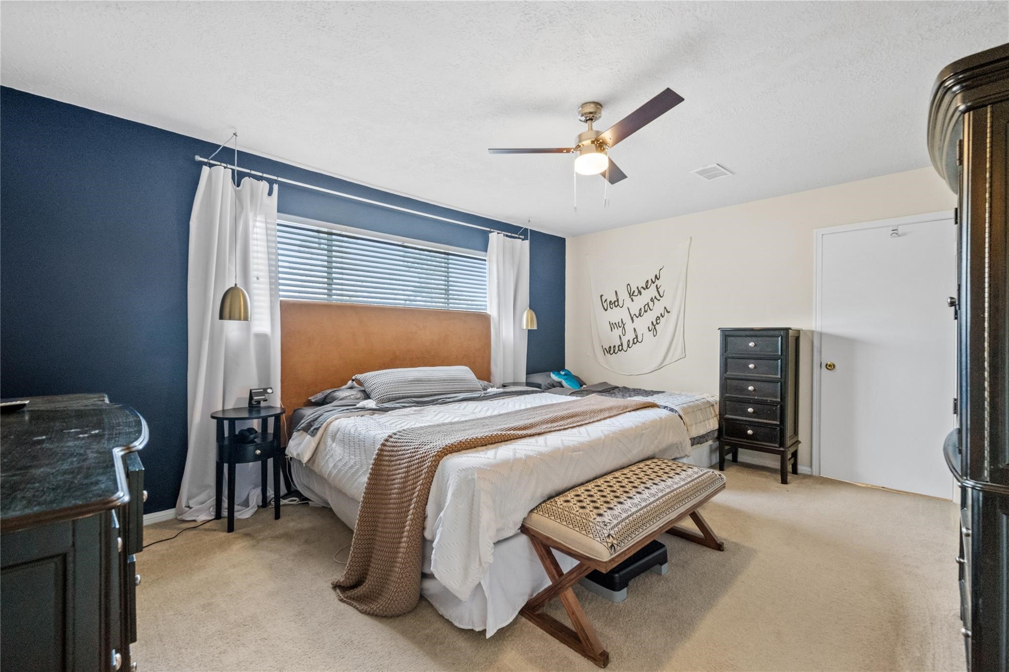 19702 Sweet Forest Lane Humble, TX 77346 - Photo 14 of 30 This bedroom features a cozy setup with a large bed, accented by a navy accent wall and warm lighting. A ceiling fan provides comfort, while ample natural light streams through a wide window. The room offers practical storage with a dresser and nightstands, creating a welcoming retreat.