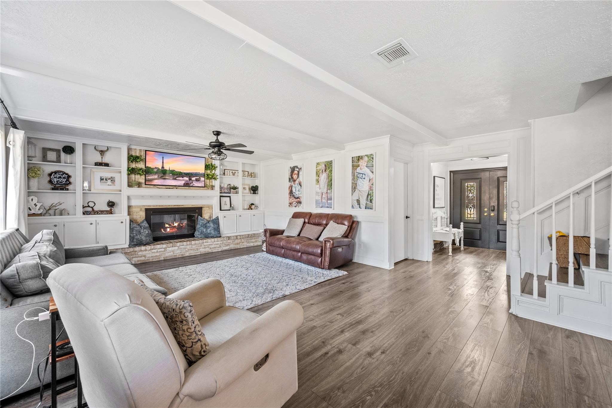 19702 Sweet Forest Lane Humble, TX 77346 - Photo 6 of 30 This spacious living room features hardwood floors, a cozy fireplace, and built-in shelving. It has a comfortable seating area with a ceiling fan and large windows for natural light. The open layout leads to a welcoming entryway and a staircase.