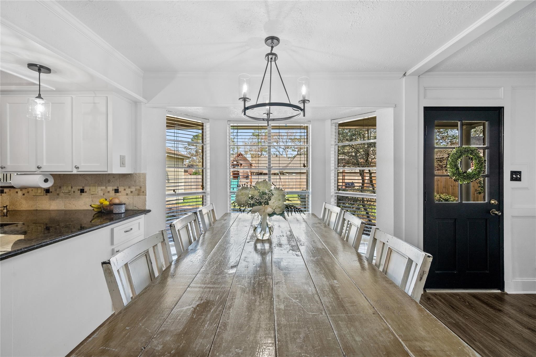19702 Sweet Forest Lane Humble, TX 77346 - Photo 10 of 30 This dining area features a long wooden table with ample seating, a stylish chandelier, and large windows offering plenty of natural light. Adjacent to a modern kitchen with white cabinets and granite countertops, it provides a welcoming space for family gatherings.