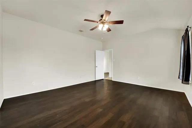 a view of an empty room with wooden floor and a ceiling fan
