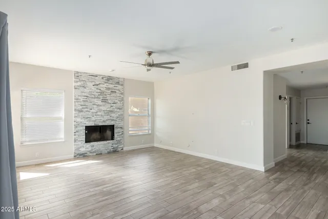 an empty room with wooden floor fireplace and windows