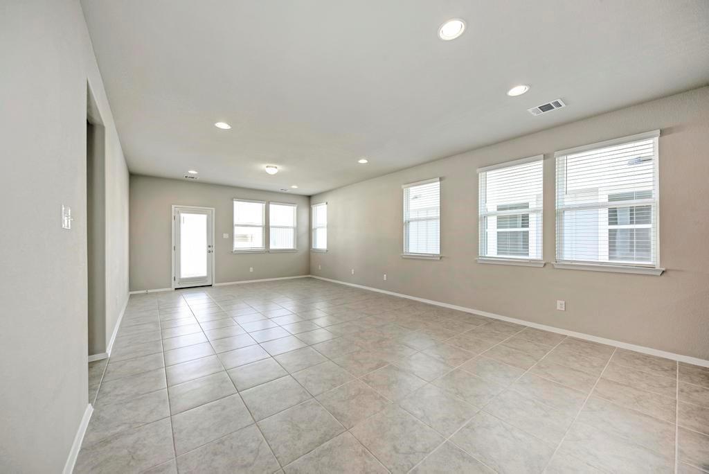 1209 Goforth Road Kyle, TX 78640 - Photo 12 of 32 Recessed lighting illuminates the spacious, neutral-toned interior, showcasing the extensive tile flooring and numerous windows.