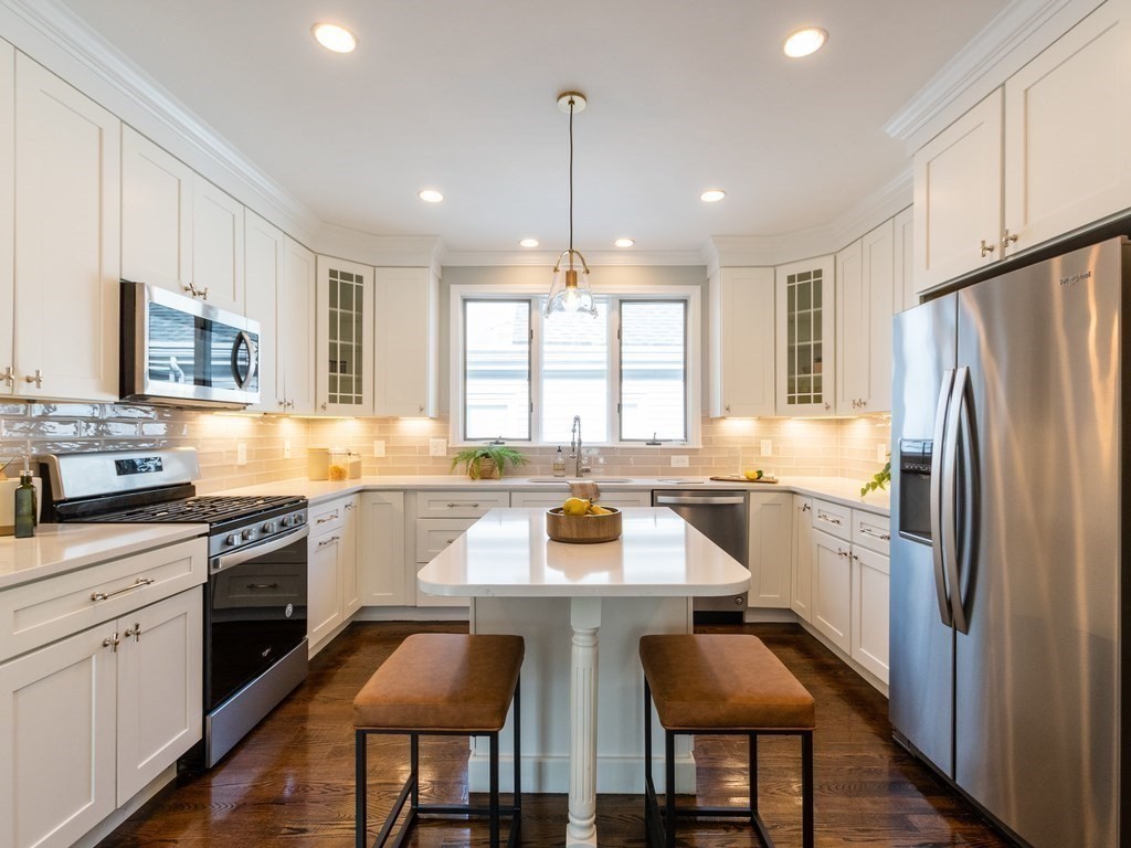 a kitchen with stainless steel appliances granite countertop a stove a sink dishwasher a refrigerator with white cabinets and wooden floor