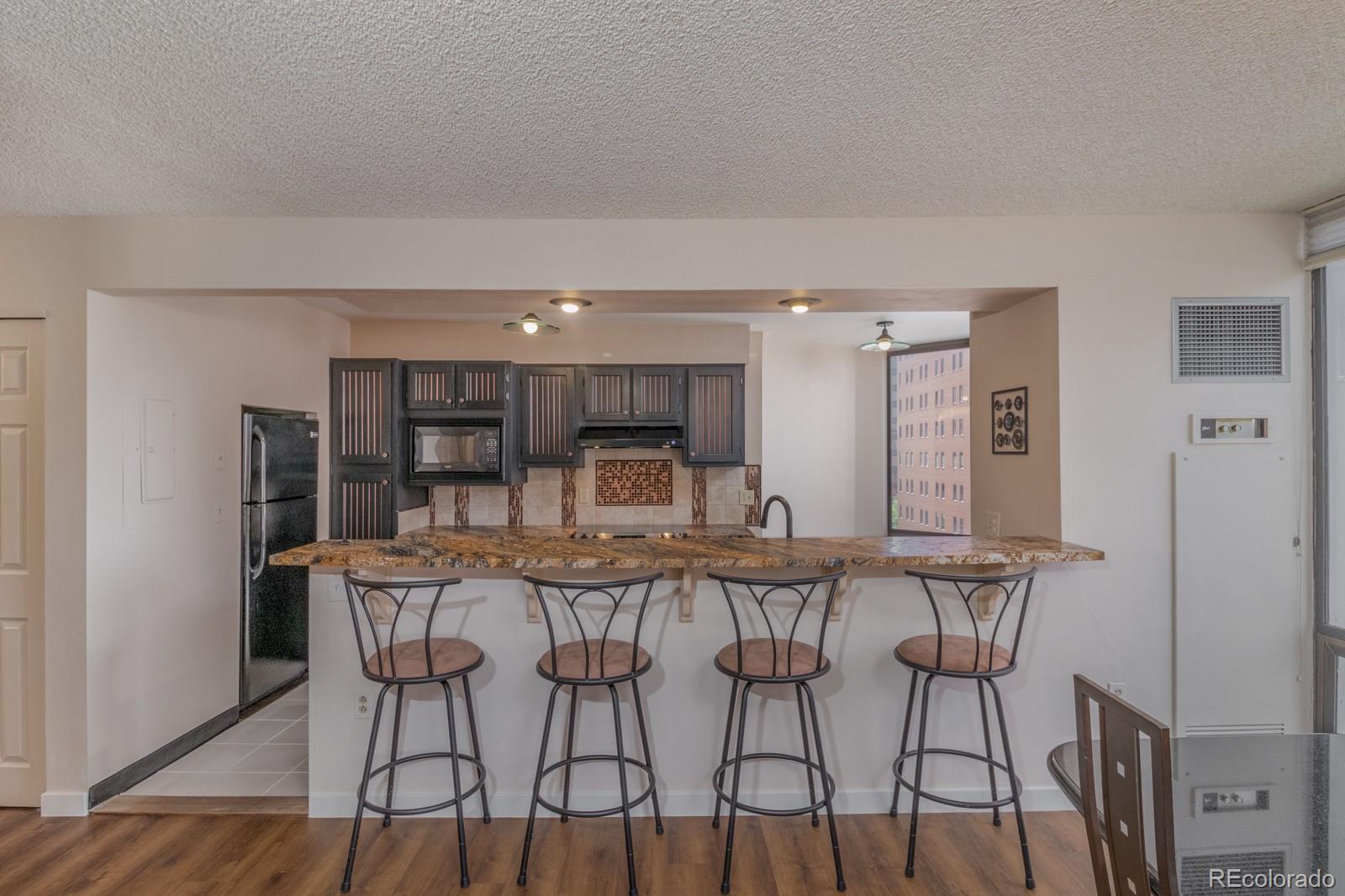 1625 Larimer Street, Unit 801 Denver, CO 80202 - Photo 5 of 33 a kitchen with stainless steel appliances kitchen island granite countertop a dining table chairs and a refrigerator