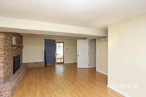 a view of an empty room with wooden floor and a fireplace