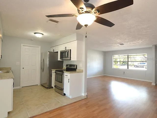 a view of a kitchen with a stove wooden floor a ceiling fan and windows