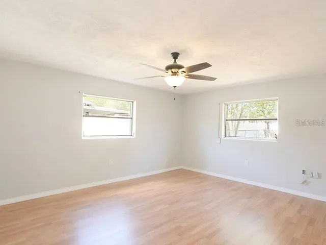 an empty room with wooden floor fan and windows