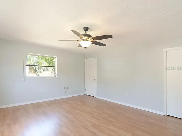 an empty room with wooden floor and ceiling fan