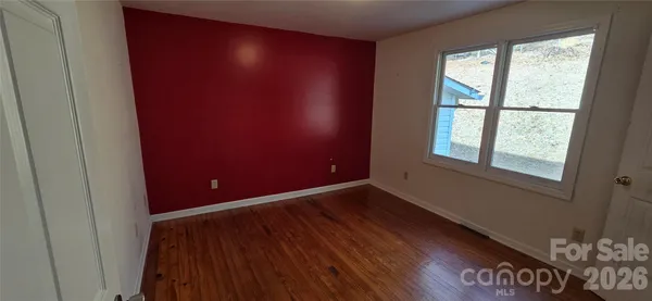 a view of an empty room with a window and wooden floor