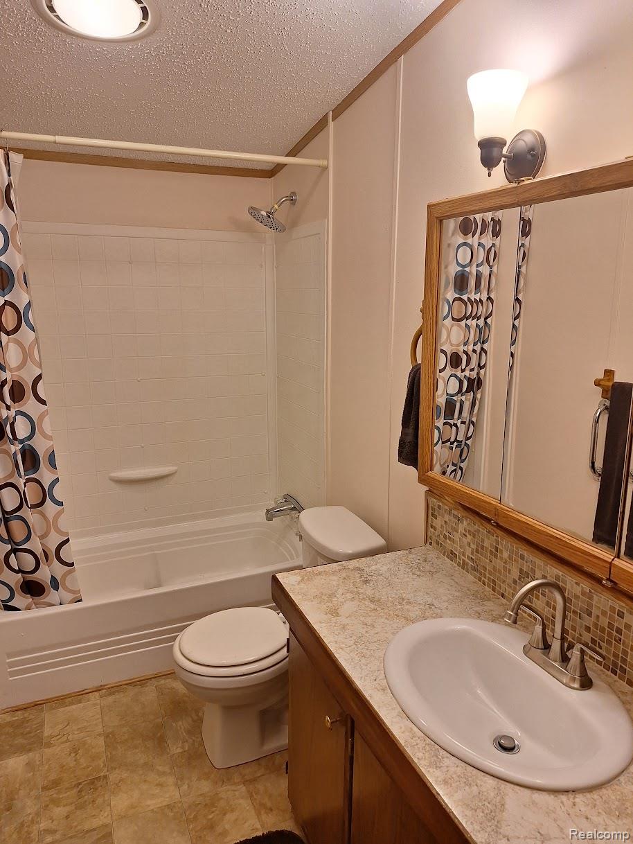 2500-mann Rd Mann Road Clarkston, MI 48346 - Photo 9 of 22 Bathroom featuring a white bathtub/shower combination with a chrome showerhead, a white toilet, and a vanity with a white oval sink, brushed nickel faucet, and a tiled backsplash