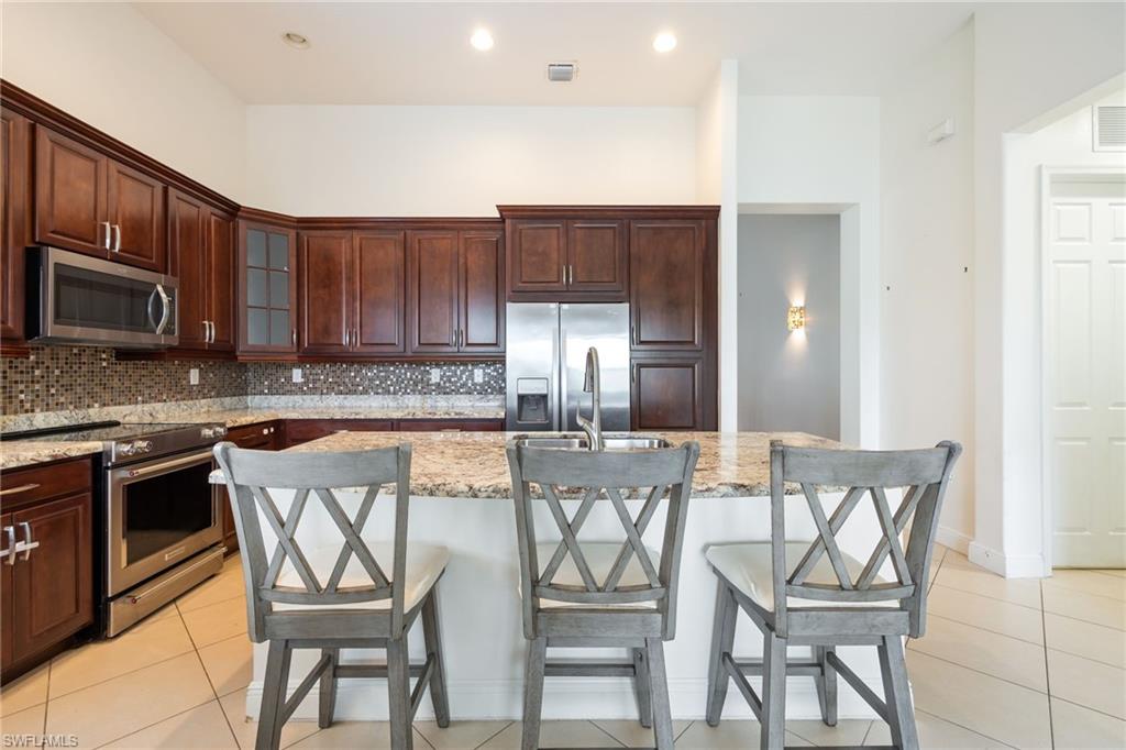 5116 Salerno Street Ave Maria, FL 34142 - Photo 11 of 36 Kitchen with stainless steel appliances, a kitchen bar, glass insert cabinets, backsplash, and recessed lighting
