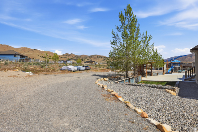 1588 West Rim Rock Drive Stockton, UT 84071 - Photo 43 of 61 Expansive gravel area bordered by natural stone, featuring an adjacent concrete patio with a playground structure and a mature tree