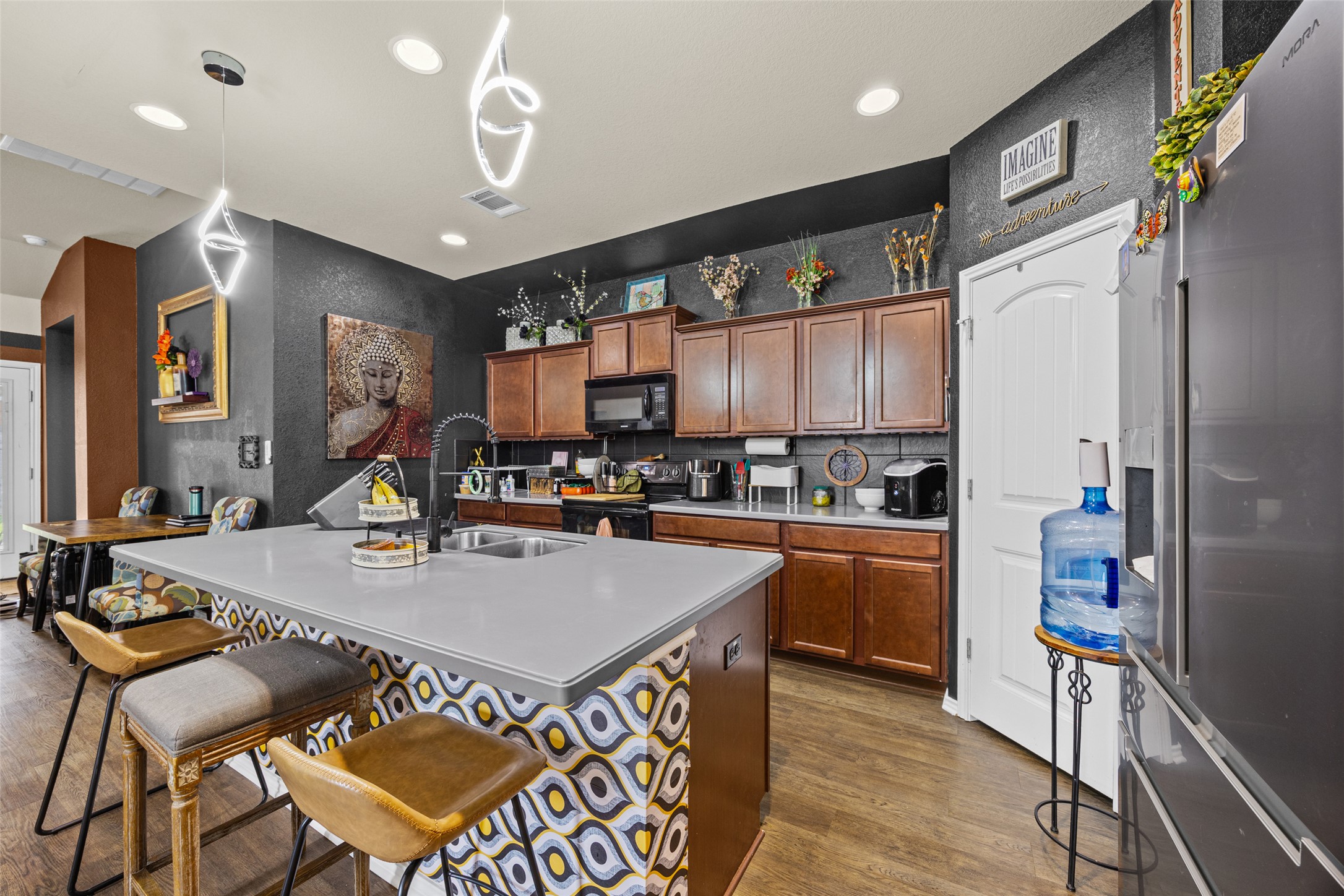 19113 Rookery Trail Pflugerville, TX 78660 - Photo 23 of 36 Modern kitchen featuring a spacious island with a light-toned countertop, sleek pendant lighting, wood-finish flooring, built-in cabinetry, and a stainless steel refrigerator