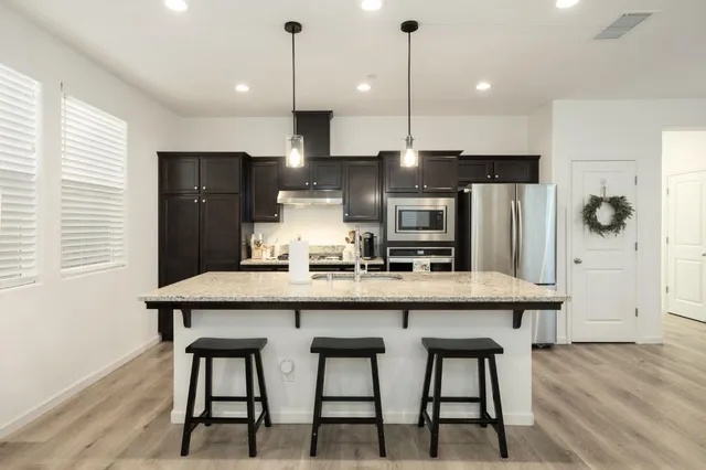 a kitchen with stainless steel appliances kitchen island granite countertop a table chairs in it and wooden floors