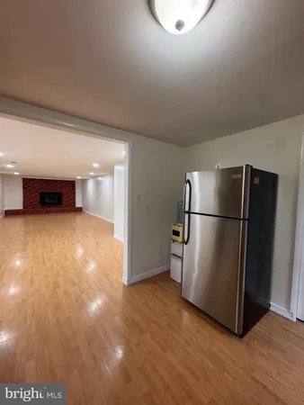a view of a refrigerator in kitchen and an empty room with wooden floor