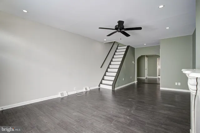 a view of an empty room with wooden floor stairs and a ceiling fan