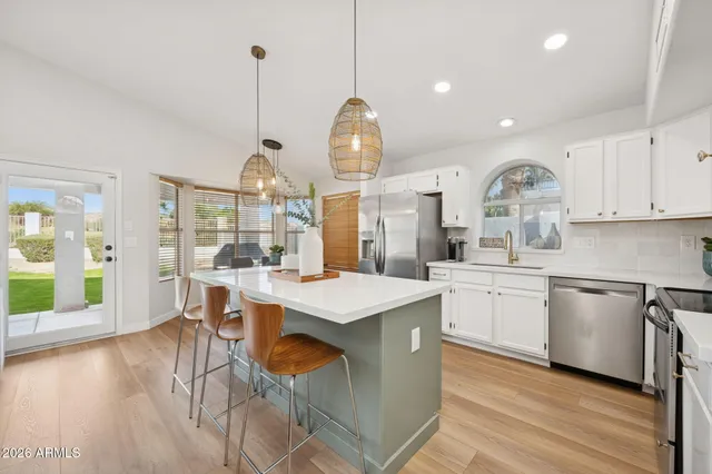a kitchen with stainless steel appliances granite countertop a stove a refrigerator a kitchen island a dining table and chairs with wooden floor