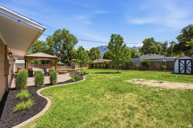 6889 South Village Road Salt Lake City, UT 84121 - Photo 31 of 44 Expansive backyard featuring a large green lawn, a dedicated patio area, a wooden gazebo, a built-in fire pit, and a detached storage shed