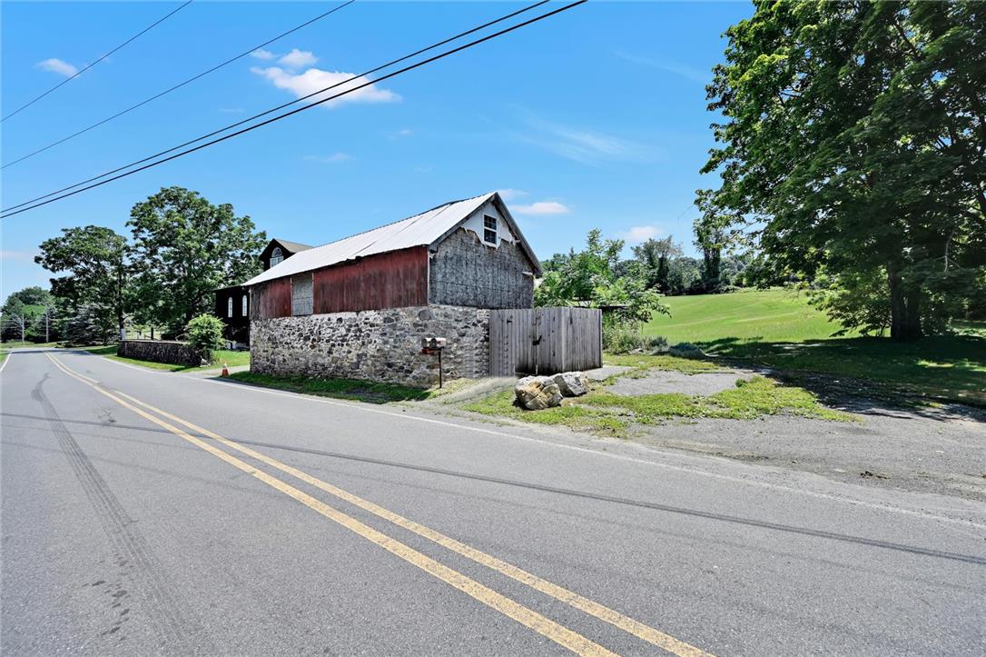 101 Conrad Road Fleetwood, PA 19522 - Photo 27 of 42 A rustic barn with a stone foundation sits beside a scenic country road, offering serene views of rolling green hills.
