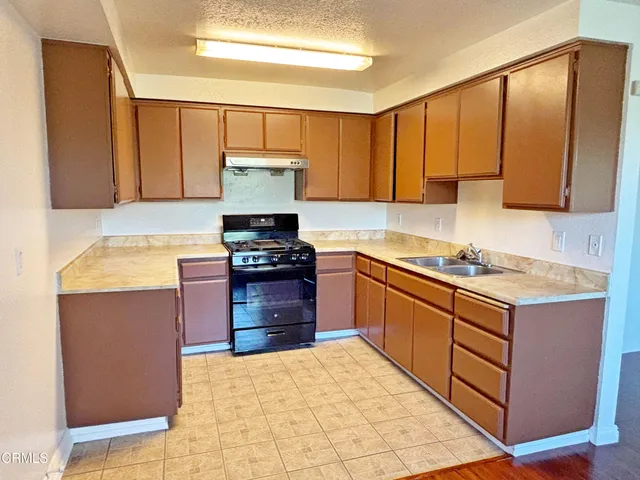 a kitchen with stainless steel appliances granite countertop a stove top oven a sink dishwasher and a refrigerator with wooden cabinets