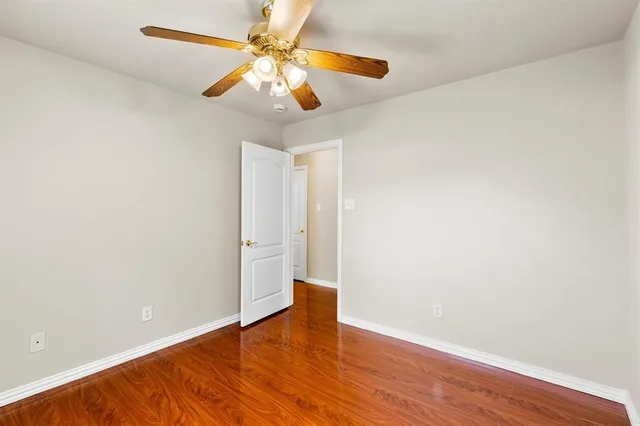 an empty room with wooden floor chandelier fan and windows