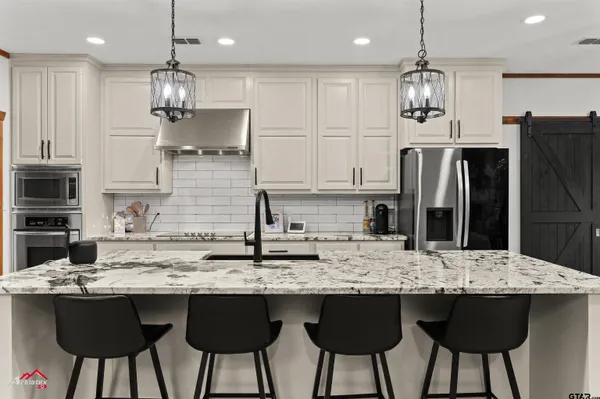 a kitchen with stainless steel appliances granite countertop a sink a stove a refrigerator and white cabinets with wooden floor