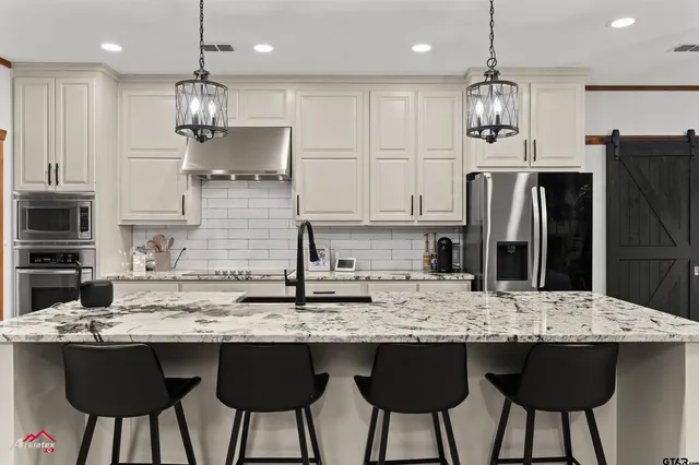 a kitchen with stainless steel appliances granite countertop a sink a stove a refrigerator and white cabinets with wooden floor