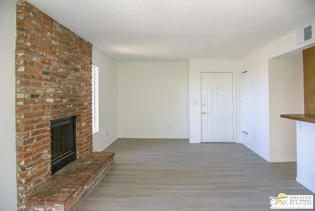 a view of an empty room with wooden floor and a fireplace