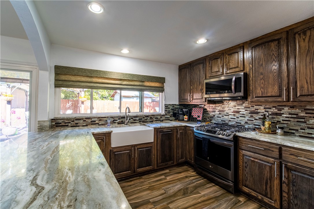 a large kitchen with stainless steel appliances granite countertop a stove top oven a sink dishwasher a dining table and chairs with wooden floor