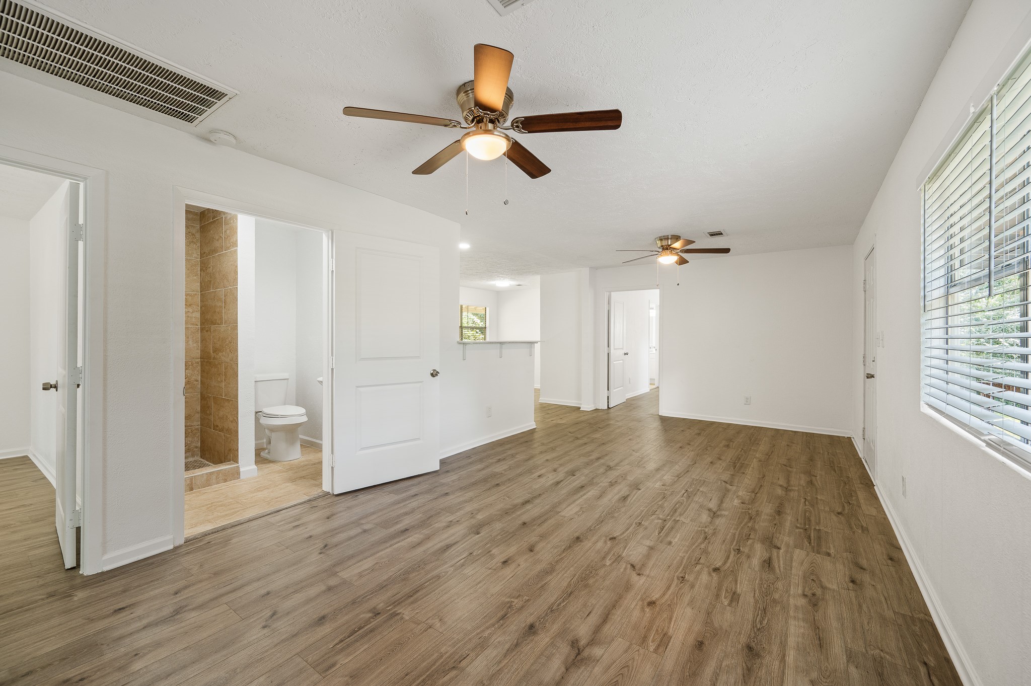 61 Hicks Loop West Cleveland, TX 77328 - Photo 19 of 38 Bright and spacious living area with wood-style flooring, ceiling fans, and a view into the kitchen. Adjacent to the living space is a modern bathroom with tiled walls.