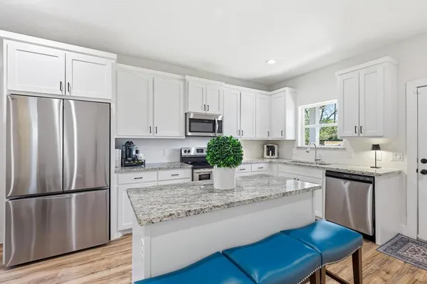 a kitchen with kitchen island granite countertop a stove a sink dishwasher a refrigerator and white cabinets with wooden floor