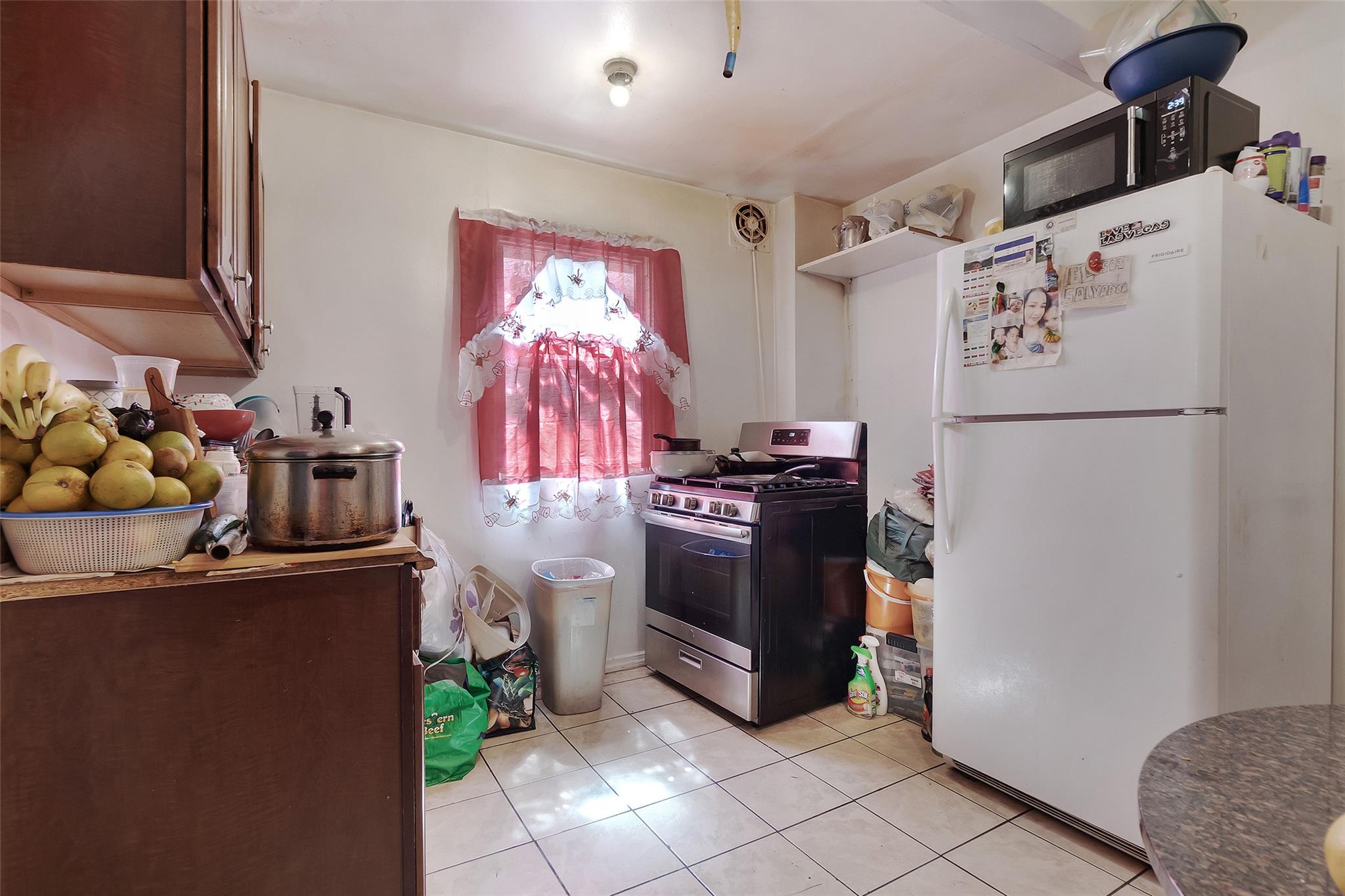 101 Baldwin Road Hempstead, NY 11550 - Photo 6 of 20 Kitchen featuring stainless steel range with gas cooktop, freestanding refrigerator, black microwave, light tile patterned flooring, and open shelves