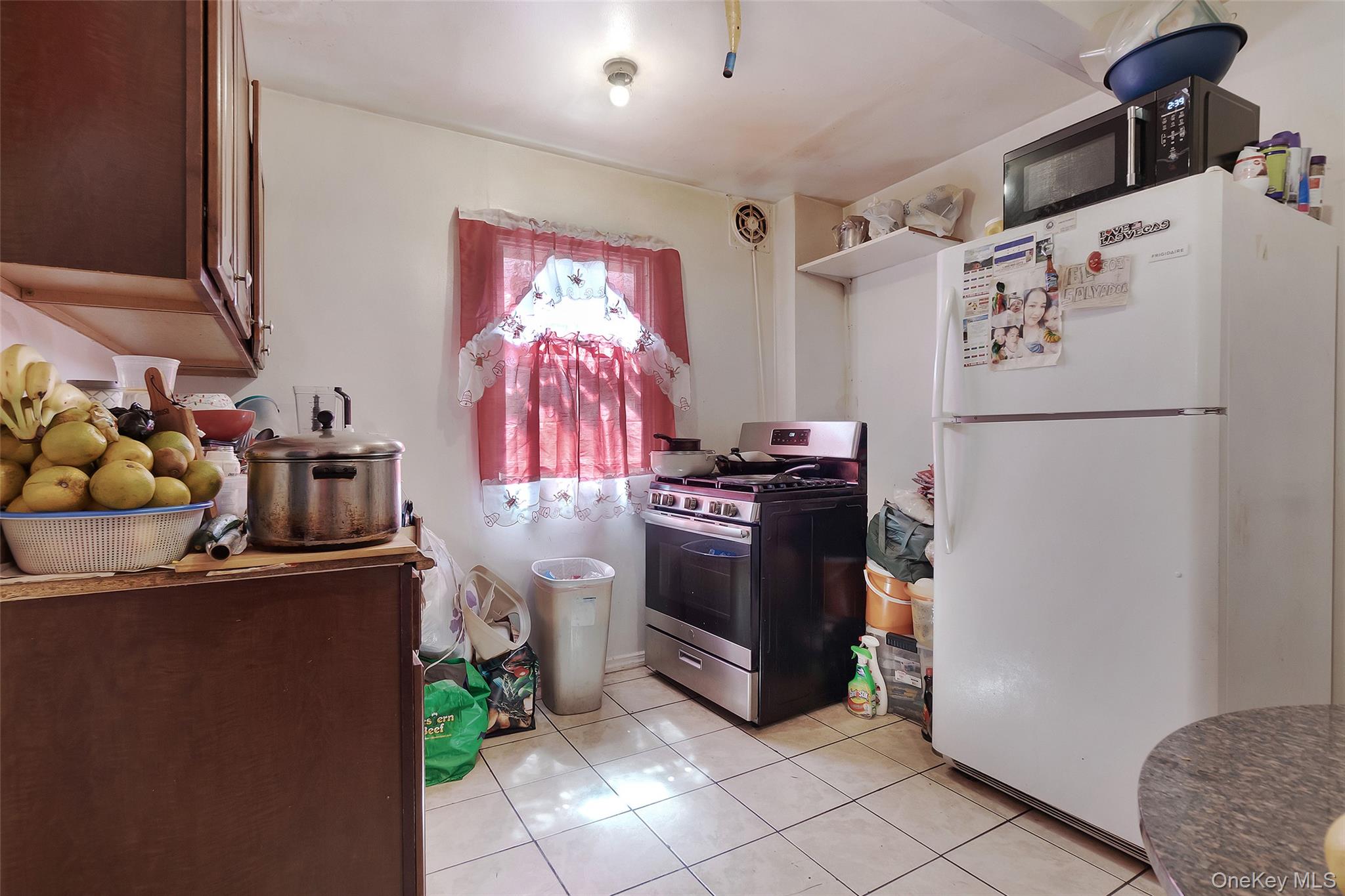 101 Baldwin Road Hempstead, NY 11550 - Photo 6 of 20 Kitchen featuring stainless steel range with gas cooktop, freestanding refrigerator, black microwave, light tile patterned flooring, and open shelves