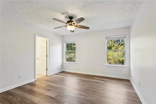 an empty room with wooden floor chandelier fan and windows