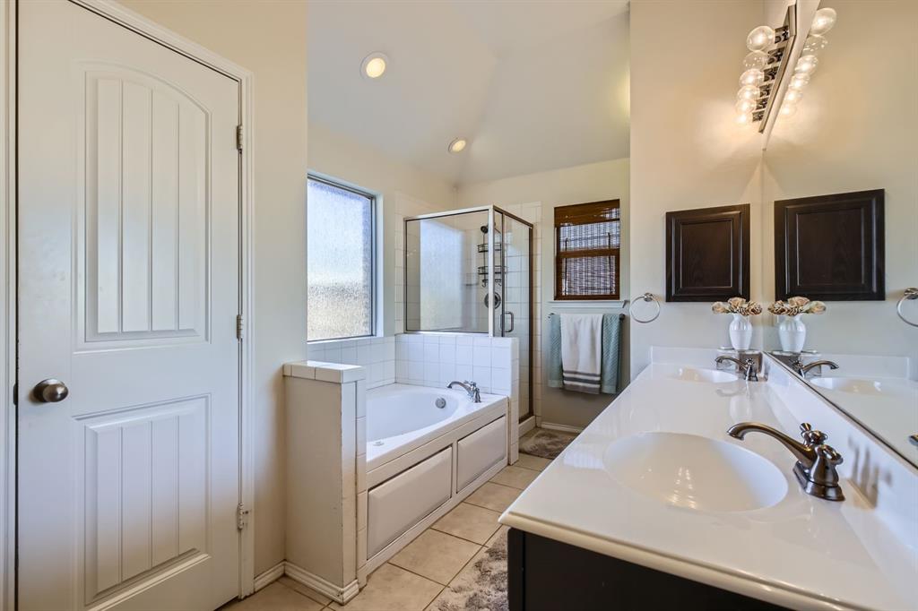 504 Thunder Trail Forney, TX 75126 - Photo 11 of 23 Bathroom featuring a double vanity with a white countertop and bronze fixtures, a built-in bathtub with white tile surround, and a glass-enclosed shower