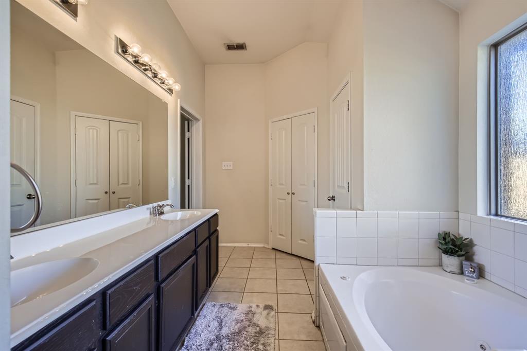 504 Thunder Trail Forney, TX 75126 - Photo 12 of 23 The bathroom features a double vanity with ample counter space, a large mirror with overhead lighting, and a built-in bathtub with tiled surround