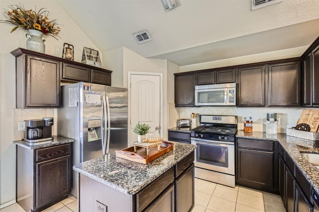 504 Thunder Trail Forney, TX 75126 - Photo 7 of 23 The kitchen features dark wood cabinetry, granite countertops, and stainless steel appliances including a refrigerator, microwave, and range