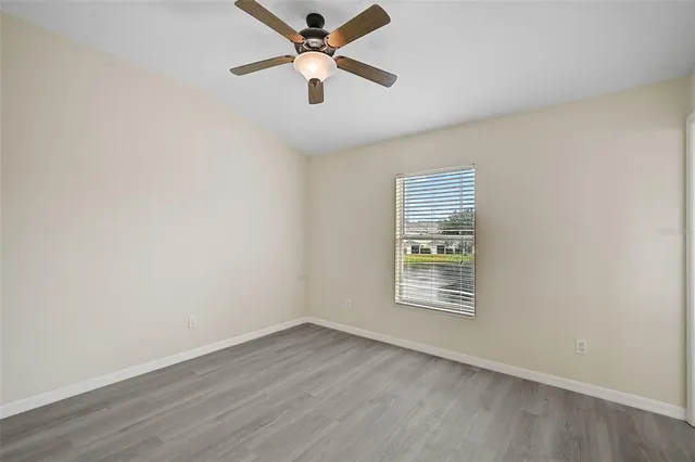 an empty room with wooden floor ceiling fan and windows